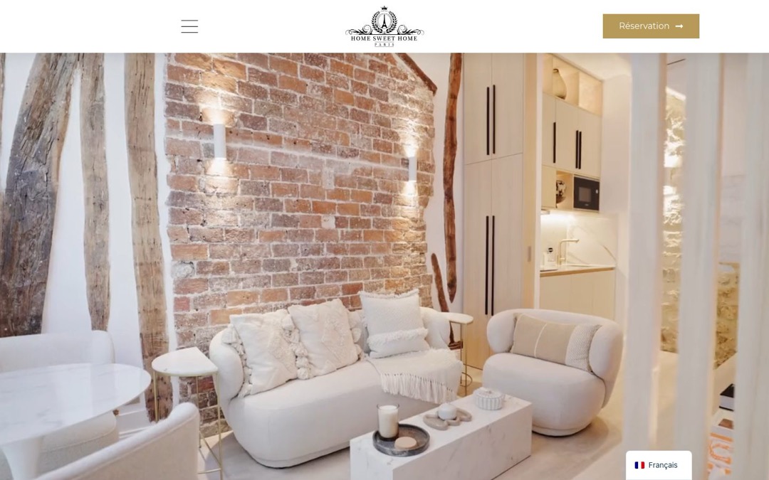Accueil du site Home Sweet Home Paris : photo d’un salon aux murs de briques apparentes, bouton « Réservation » en haut à droite et menu de langue « Français » en bas à droite