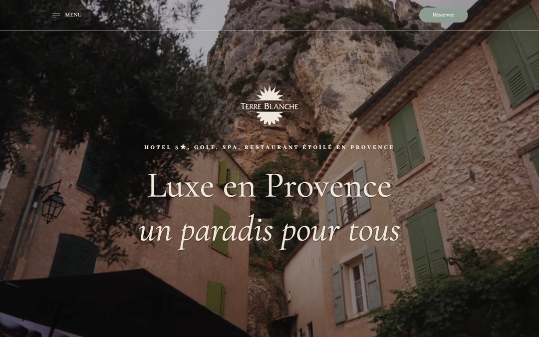 Accueil du site de Terre Blanche : vidéo plein écran d’un village provençal aux volets verts devant une falaise, logo au centre, menu à gauche, bouton « Réserver » à droite, titre « Luxe en Provence, un paradis pour tous »