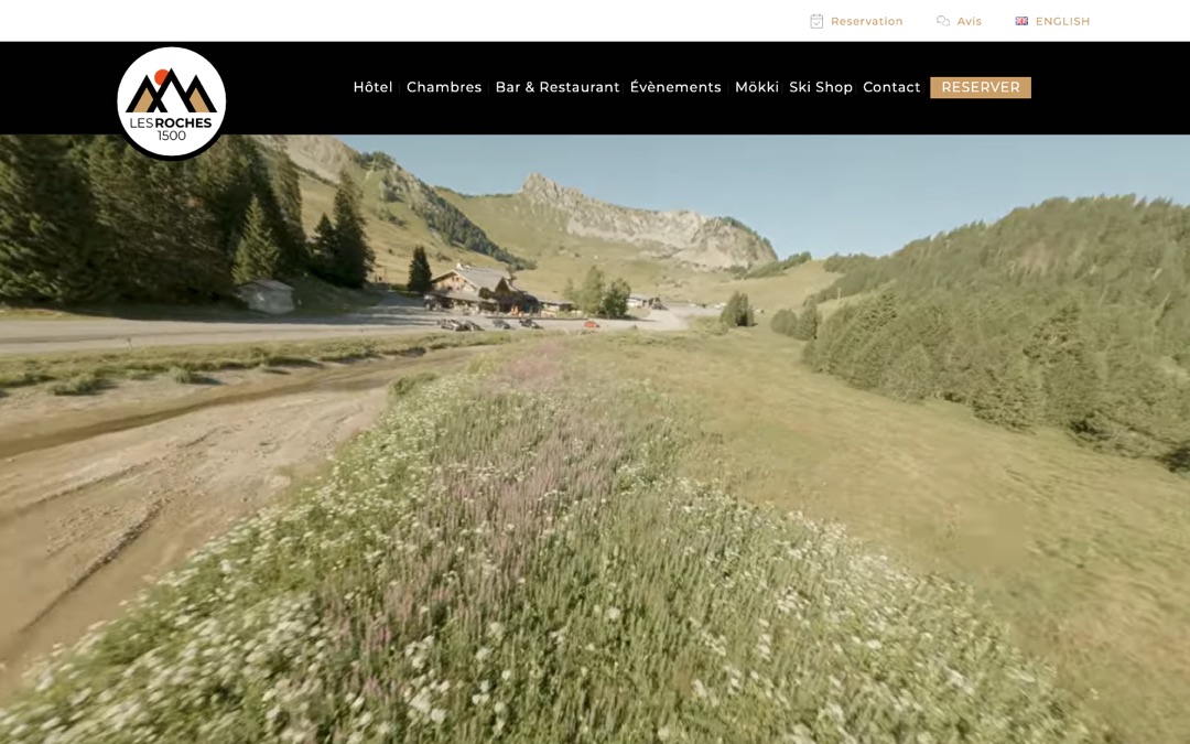 Accueil du site des Roches 1500 : vidéo de montagne, menu noir avec le bouton « Réserver » et barre « Réservation, Avis, English »