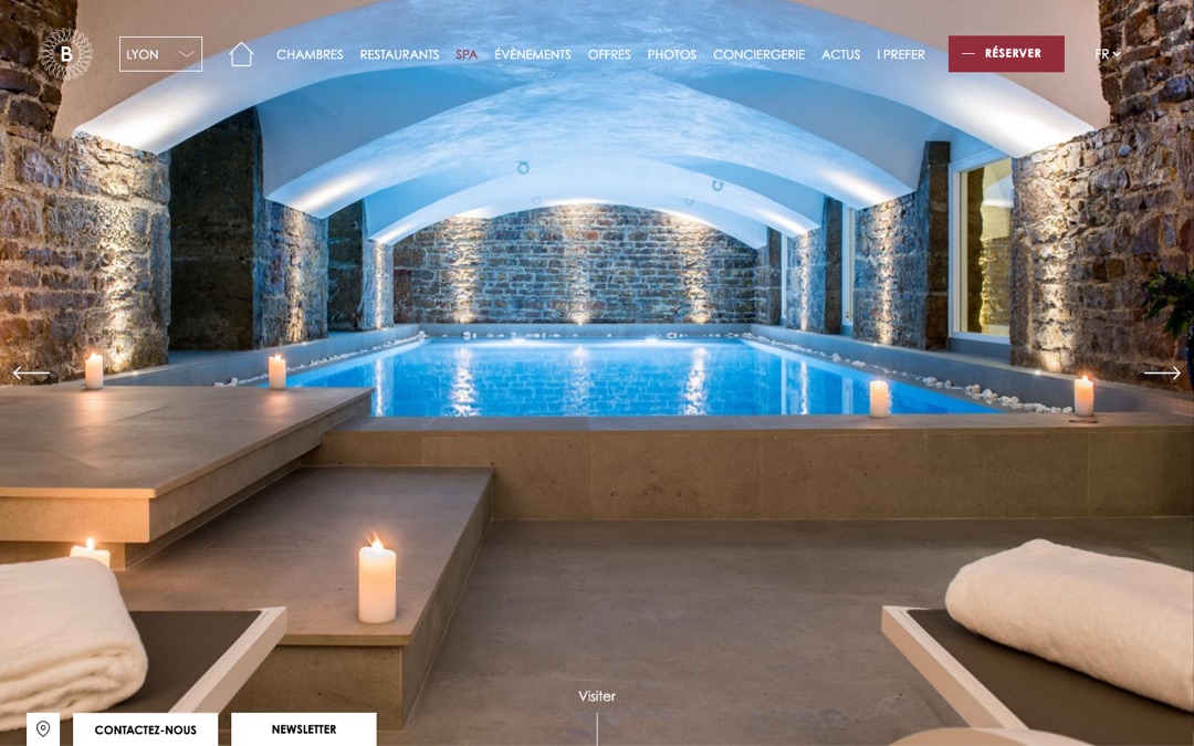 Page du spa de l’hôtel Boscolo à Lyon : photo plein écran d’un bassin sous une voûte en pierre éclairée de bougies