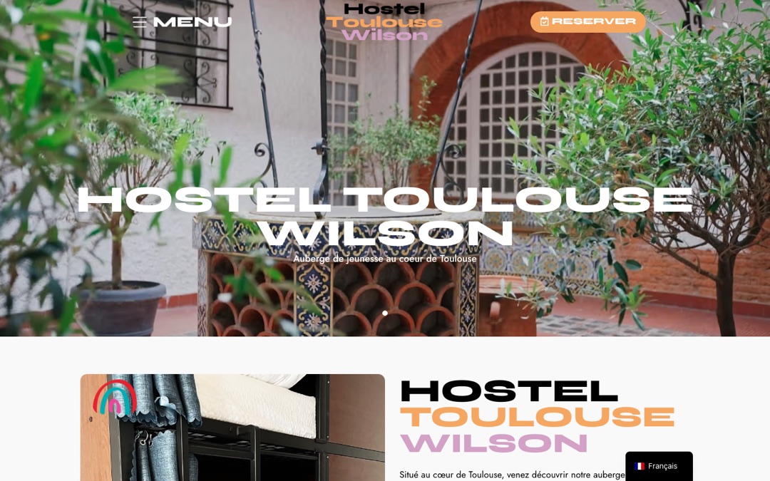 Accueil du site de l’Hostel Toulouse Wilson : cour fleurie, menu à gauche, logo au centre et bouton « Réserver » en haut à droite