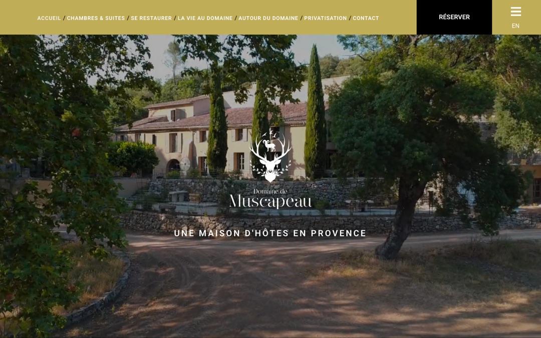 Accueil du site du Domaine de Muscapeau : maison de pierre sous les arbres, menu en bandeau doré et bouton noir « Réserver » en haut à droite
