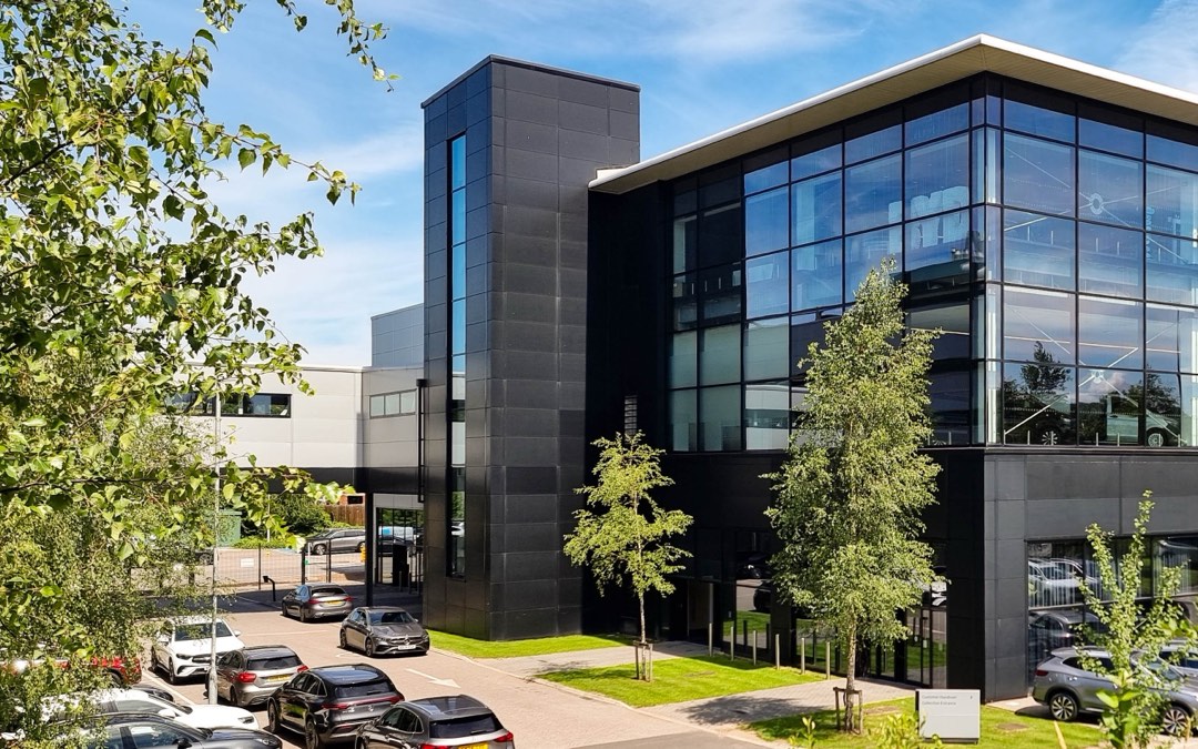 Façade vitrée d’une concession automobile, avec des véhicules garés devant le bâtiment et de jeunes arbres plantés le long du parking