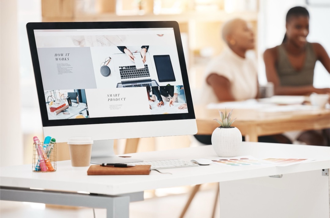 Écran d’ordinateur sur un bureau de créatifs, affichant une mise en page avec des titres en capitales et du texte en petit corps