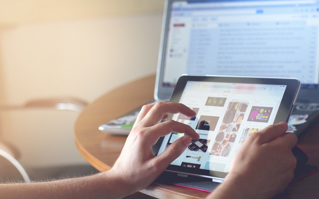 Les mains d’une personne qui fait défiler une page sur une tablette, devant un ordinateur portable