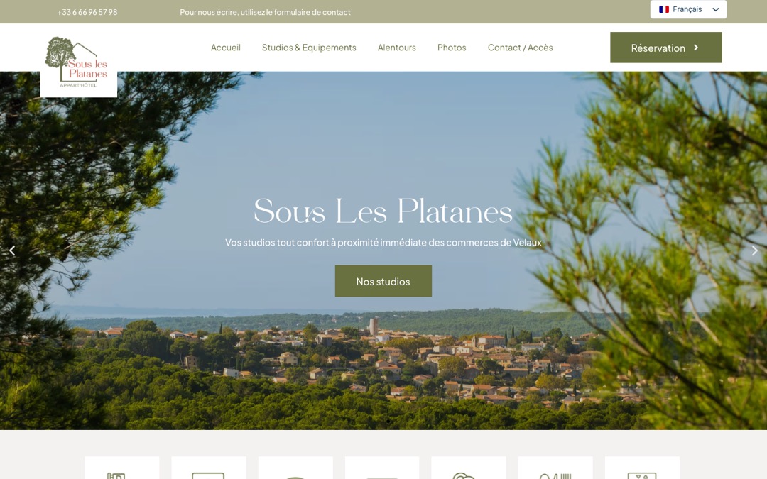 Accueil du site de l’appart’hôtel Sous Les Platanes : vue du village de Velaux à travers les pins, bouton « Nos studios », menu et bouton « Réservation » en haut à droite