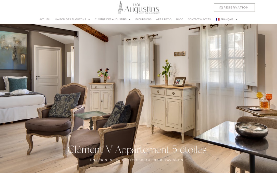 Salon d’une suite du site Augustins 1261 à Avignon : lit, fauteuils anciens et fenêtres sur les toits
