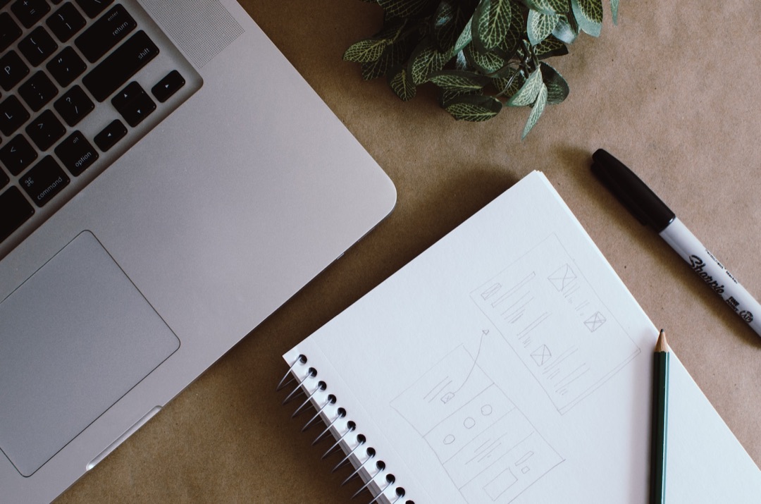 Un ordinateur portable, un carnet de croquis de pages web et une plante sur un bureau