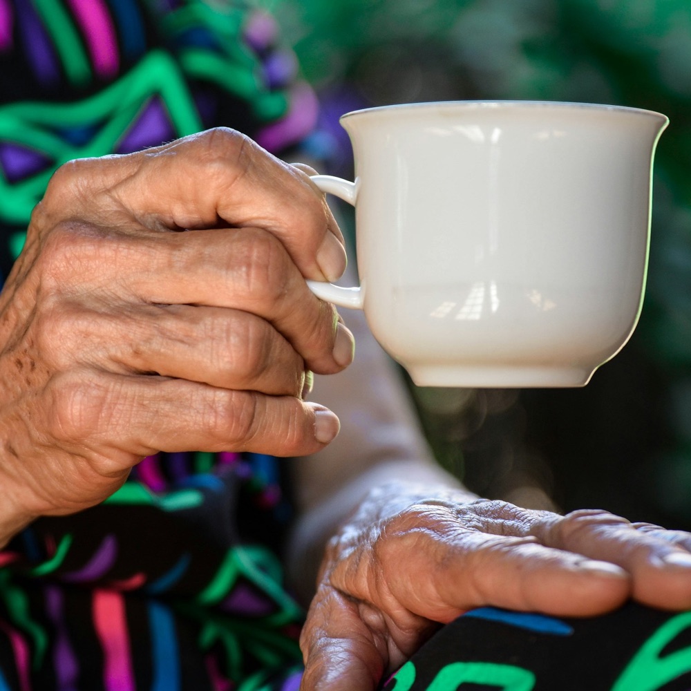 Les mains d’une personne âgée, l’une tenant une tasse blanche