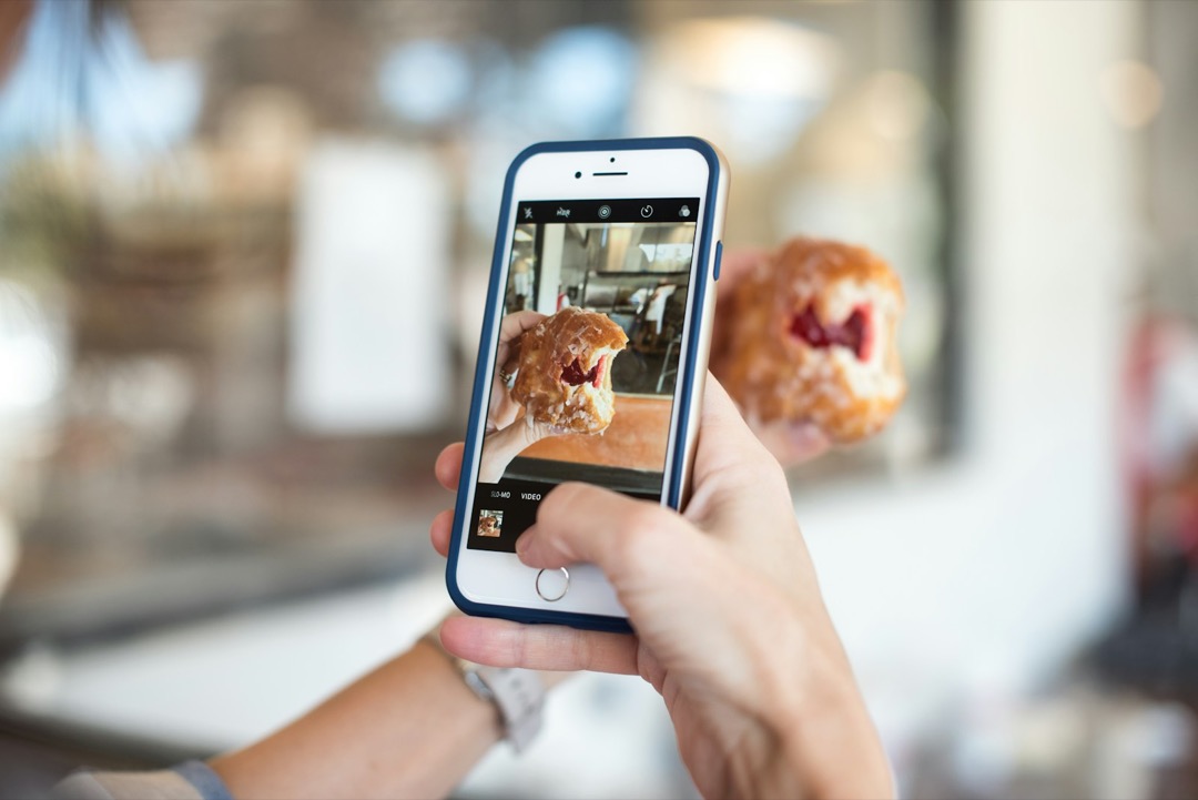 Une main photographie une pâtisserie avec un téléphone, dans un café