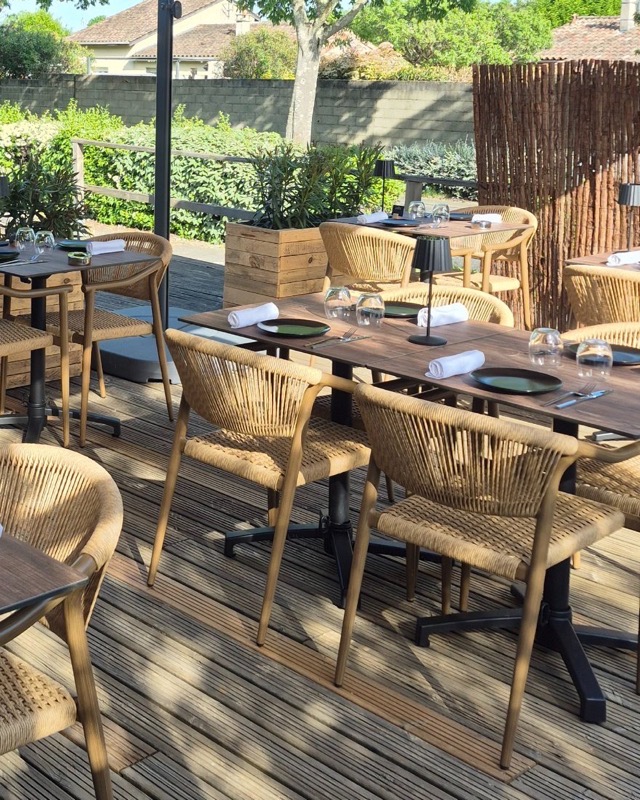 Terrasse de restaurant en bois avec des tables dressées et des fauteuils en corde tressée