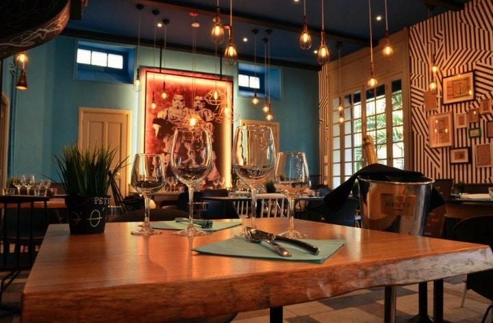 Table en bois dressée de verres à pied dans une salle de restaurant aux lumières suspendues