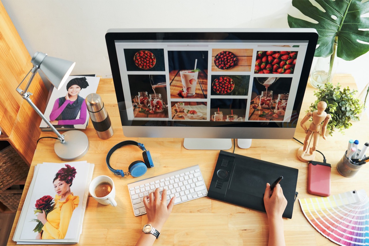 Poste de travail vu du dessus&nbsp;: un grand écran affiche une planche de photos de desserts aux fraises, à côté d’un clavier et d’une tablette graphique