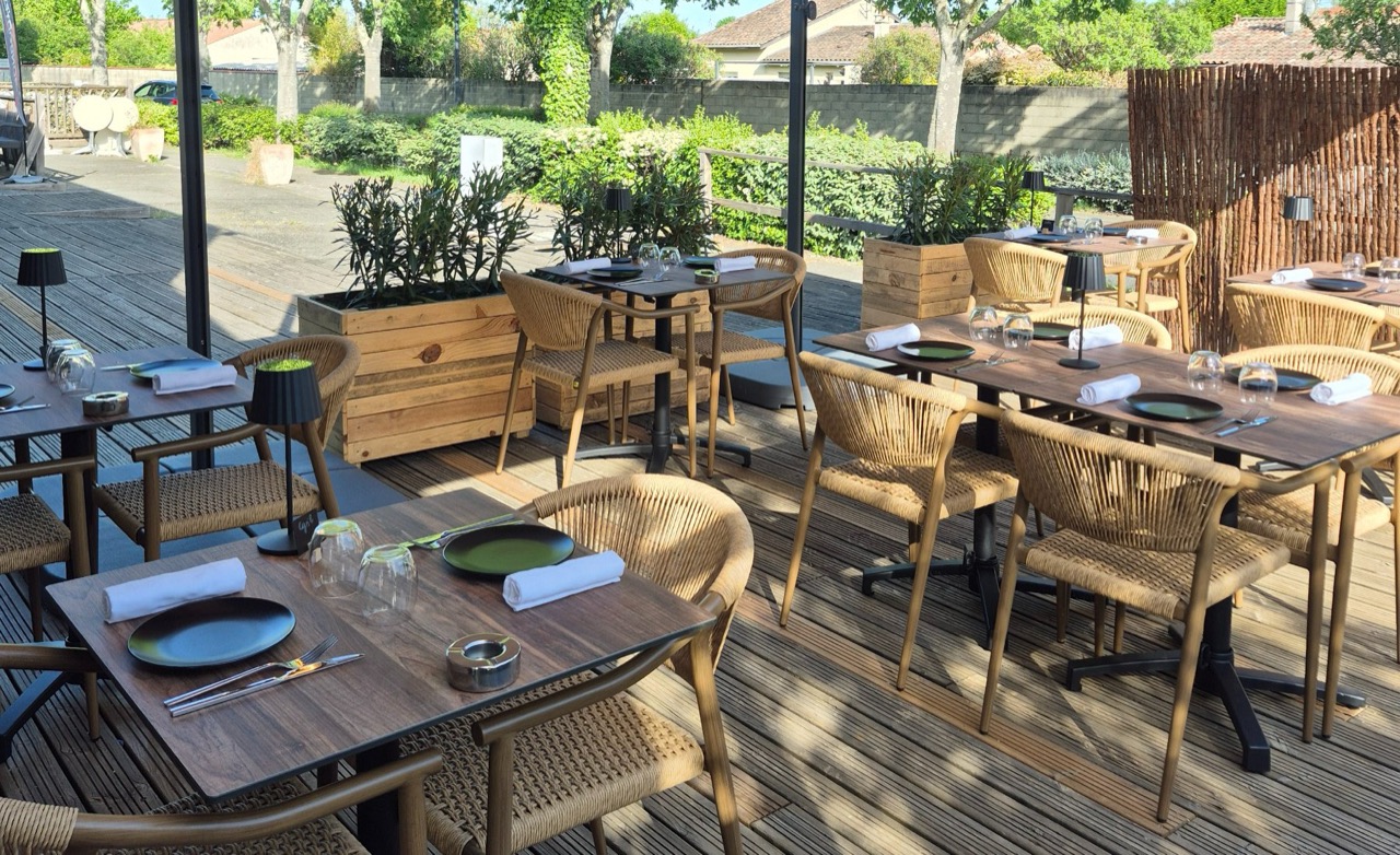 Terrasse d’un restaurant avec tables en bois, fauteuils en corde tressée et grands parasols